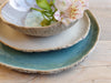 Stack of ceramic plates with a small bowl and flowers on a wooden surface