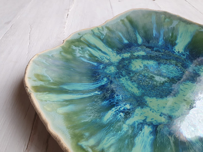 Close-up of a ceramic plate with green and blue glaze on a light wooden surface