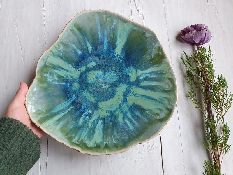 Hand holding a ceramic plate with a blue and green glaze